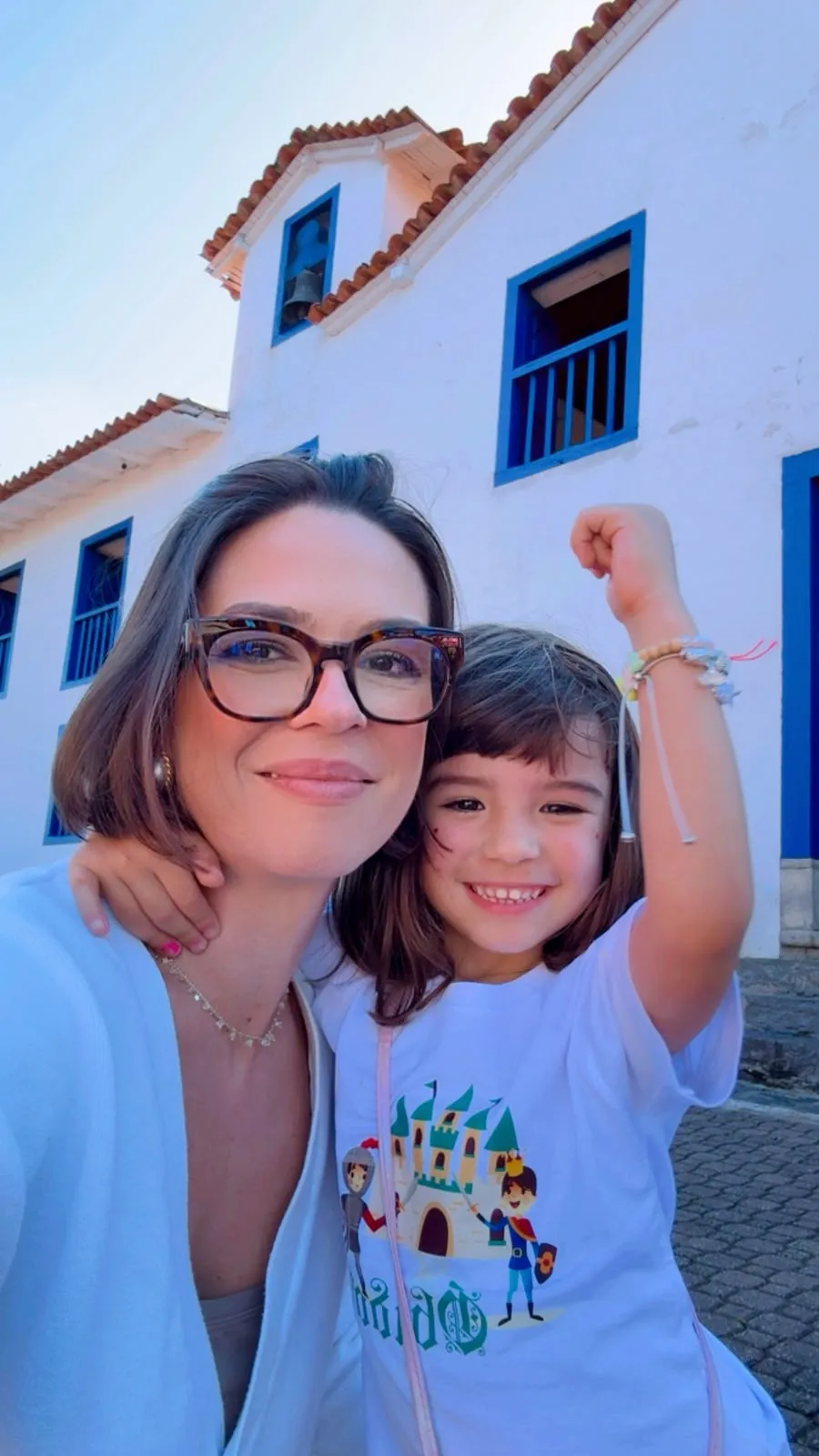 Nicole com a filha no colo diante de um casarão colonial