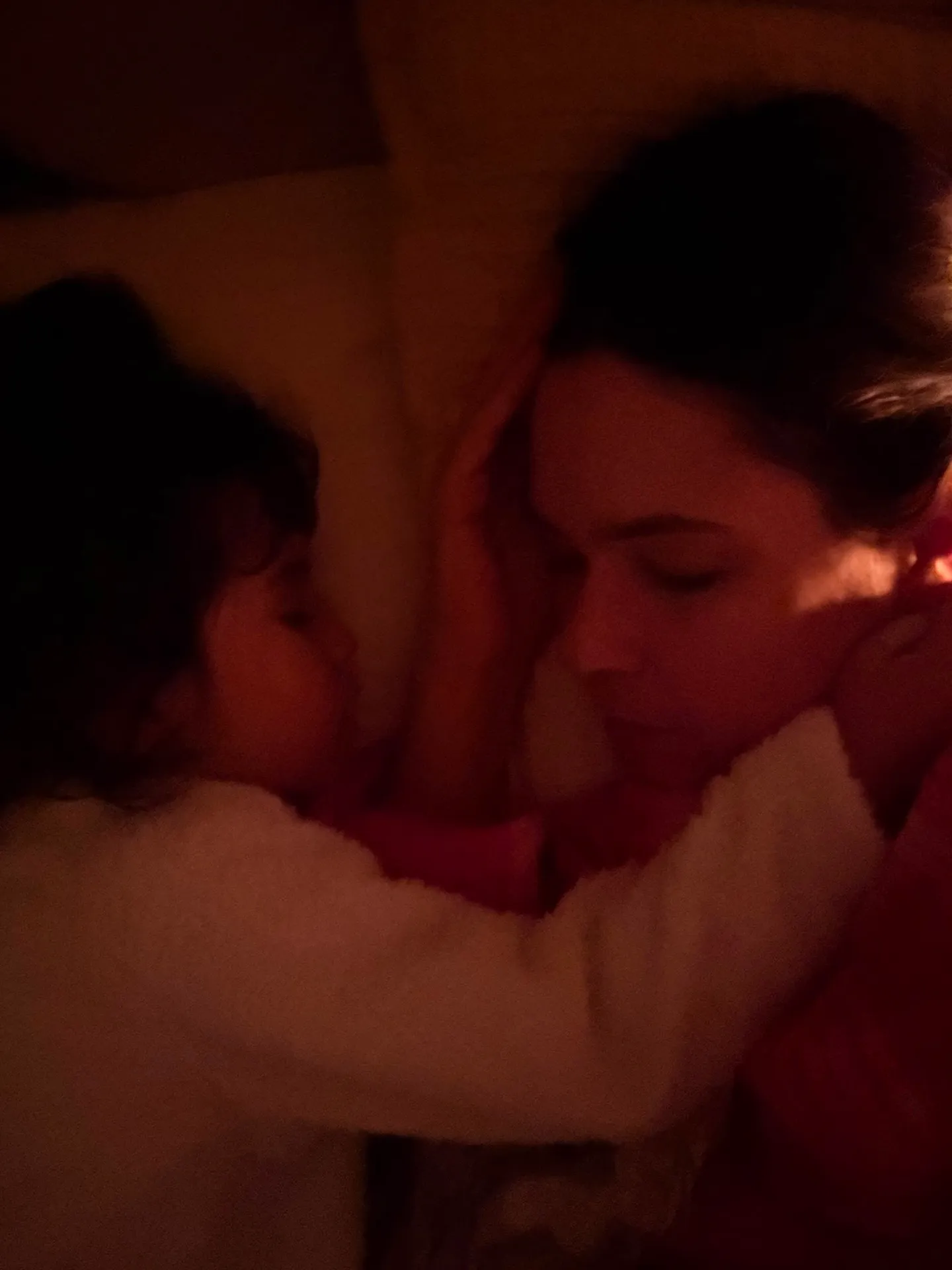 Nicole deitada com a filha no colo, à meia-luz de um abajur